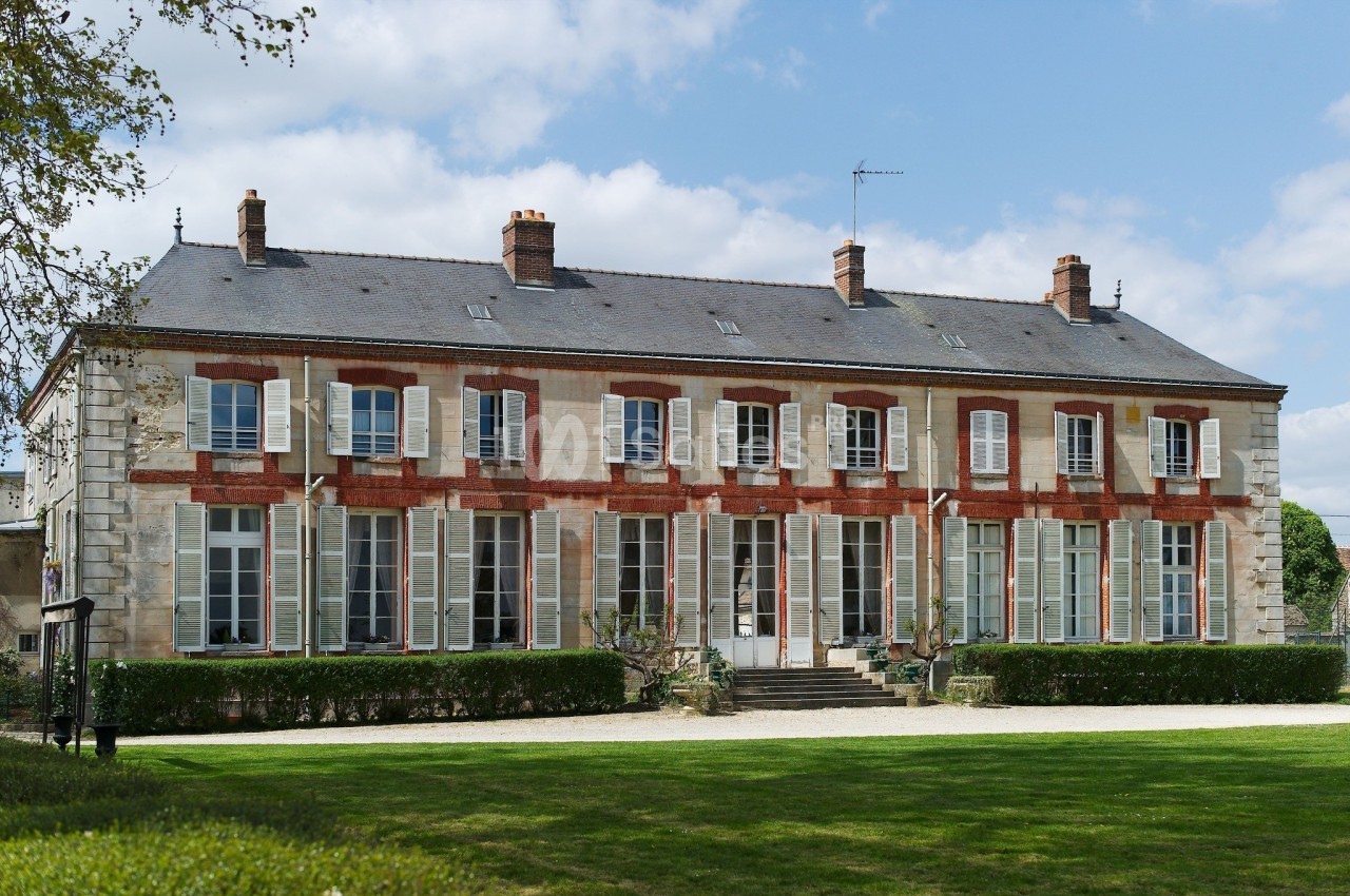 Façade d'un grand bâtiment en pierre et briques rouges avec de nombreuses fenêtres, entouré d'un jardin.