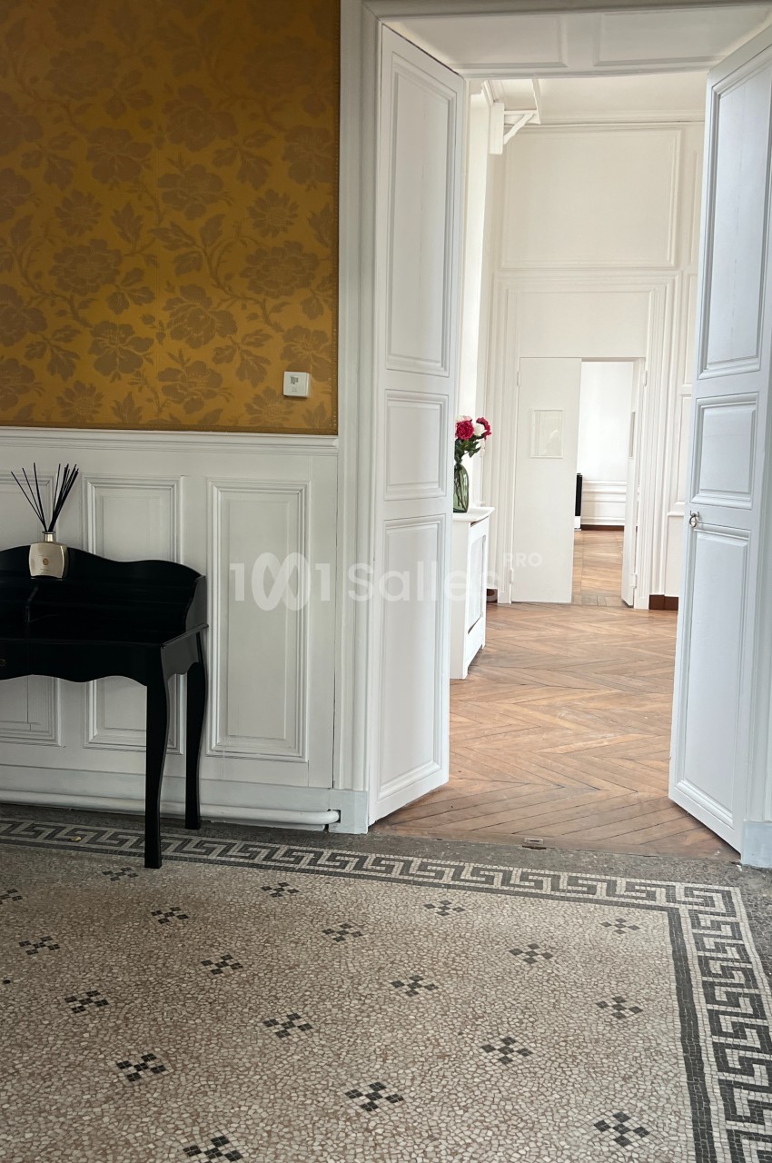 Vue d'un intérieur lumineux avec un sol en mosaïque, un bureau noir et une enfilade de portes ouvertes.