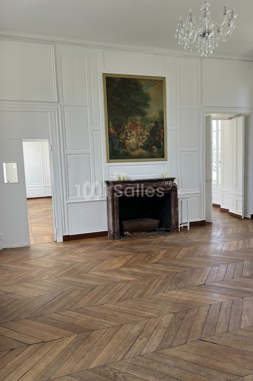 Salle lumineuse avec parquet en bois, cheminée en marbre, tableau au mur et moulures blanches sur les murs.