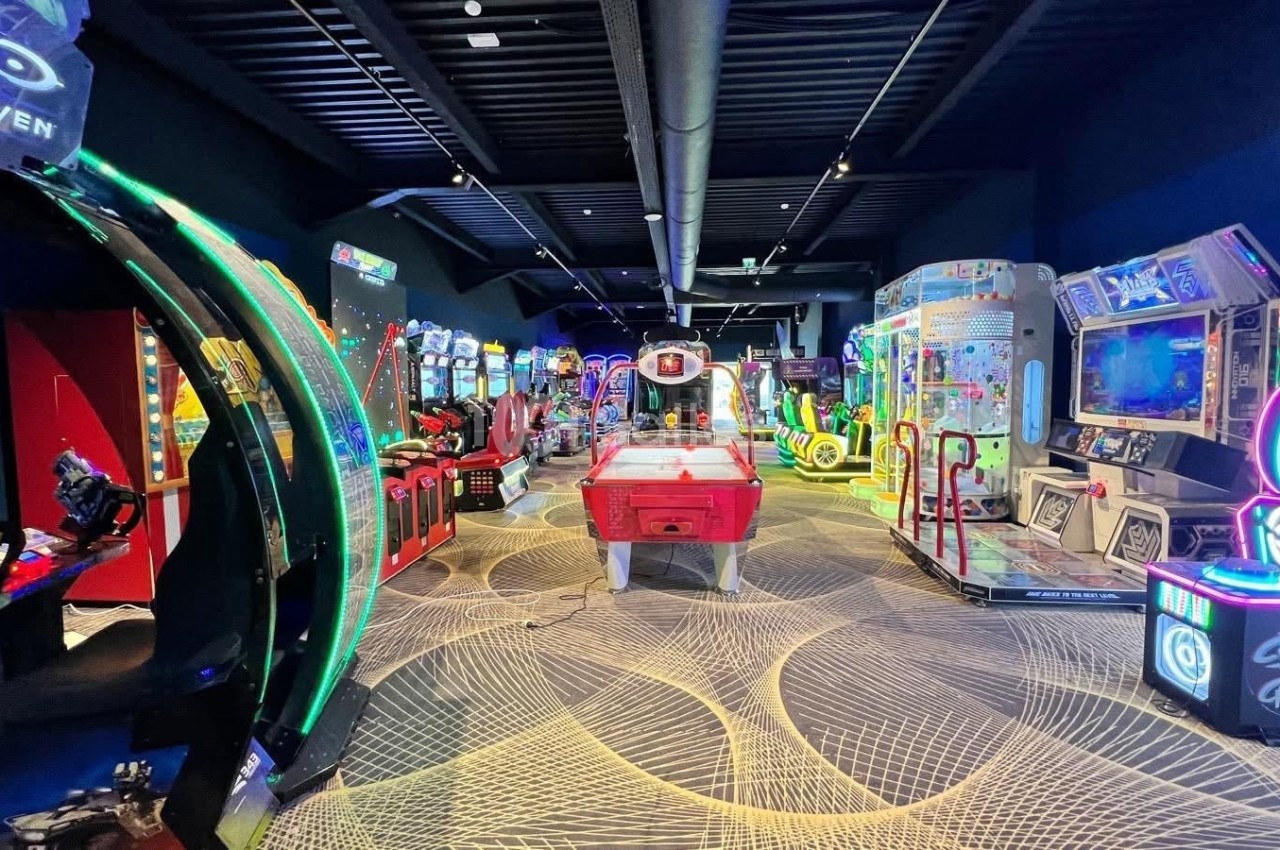 Salle d'arcade avec divers jeux vidéo, machines interactives et éclairages colorés dans un espace moderne.