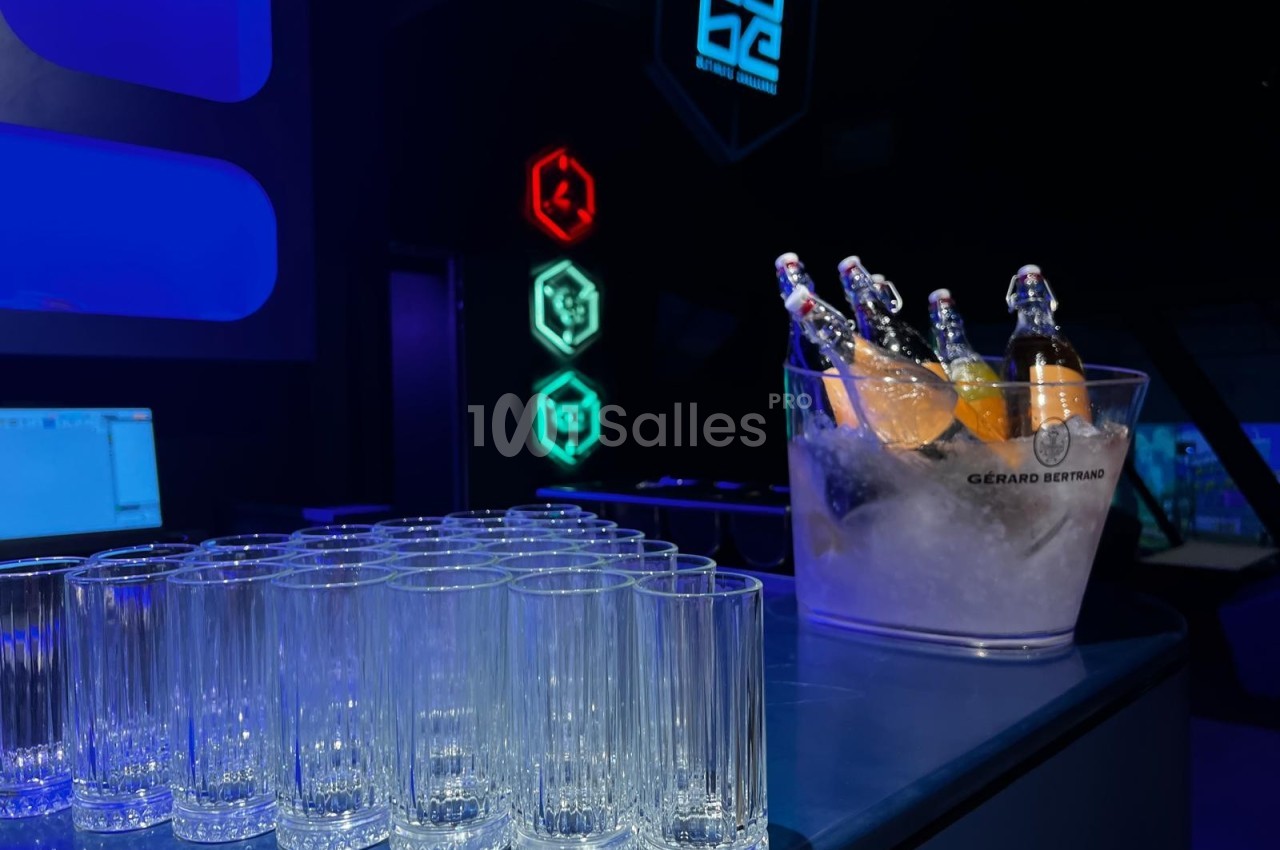 Des verres vides alignés sur un comptoir avec un seau rempli de bouteilles dans un décor lumineux.