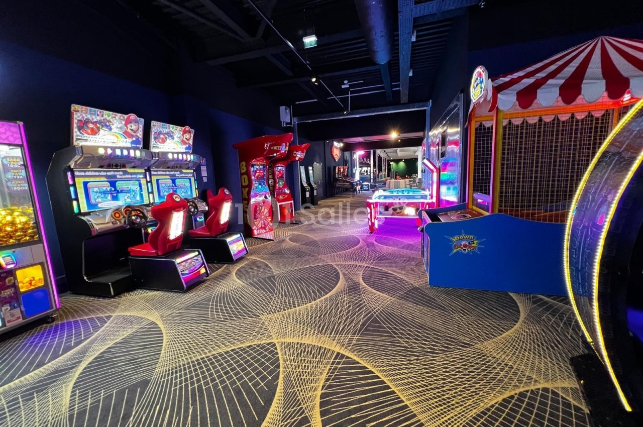 Salle de jeux d'arcade avec machines interactives, flippers, baby-foot et décorations lumineuses colorées.