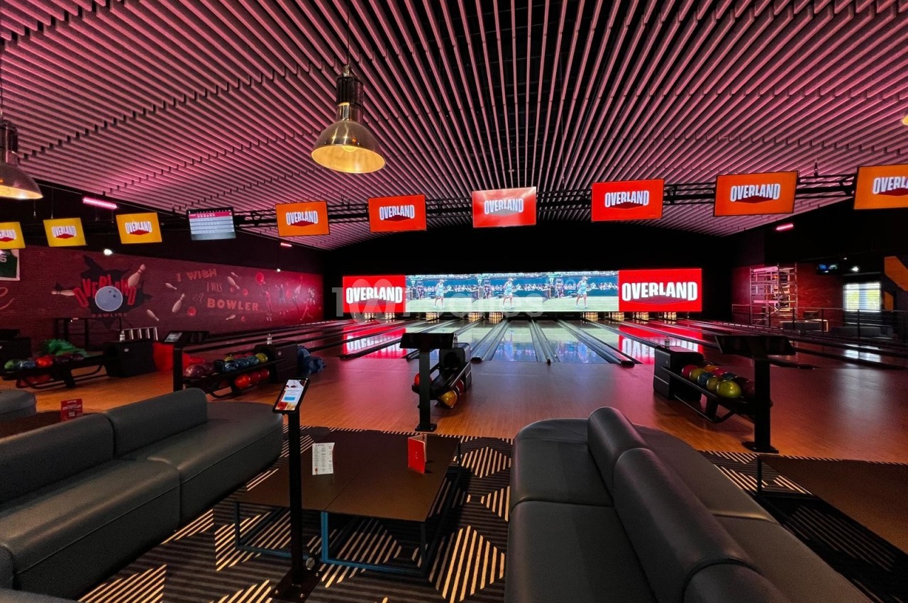 Salle de bowling moderne avec plusieurs pistes, éclairage coloré et écrans affichant le logo ’Overland’.