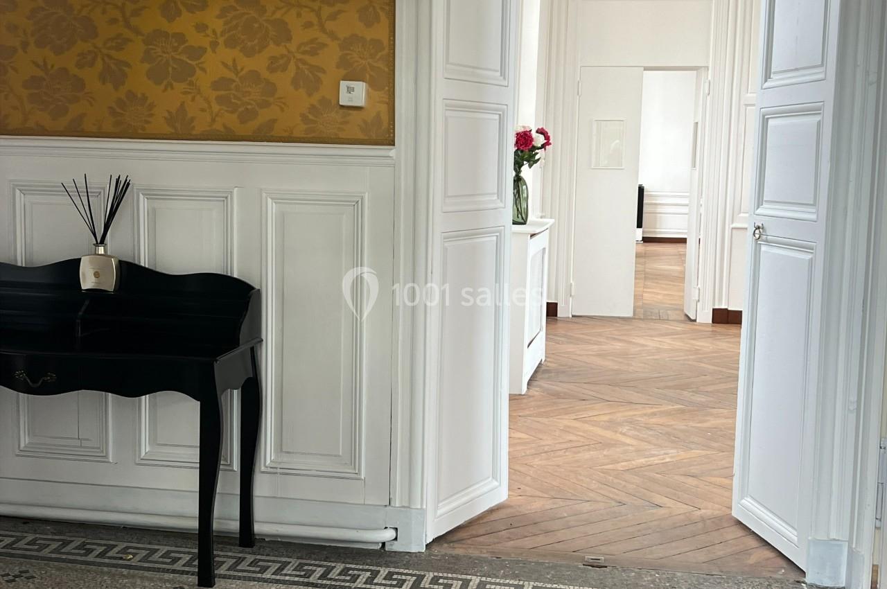 Vue intérieure d'un appartement avec parquet en bois, murs blancs, papier peint jaune et une table noire avec un diffuseur.