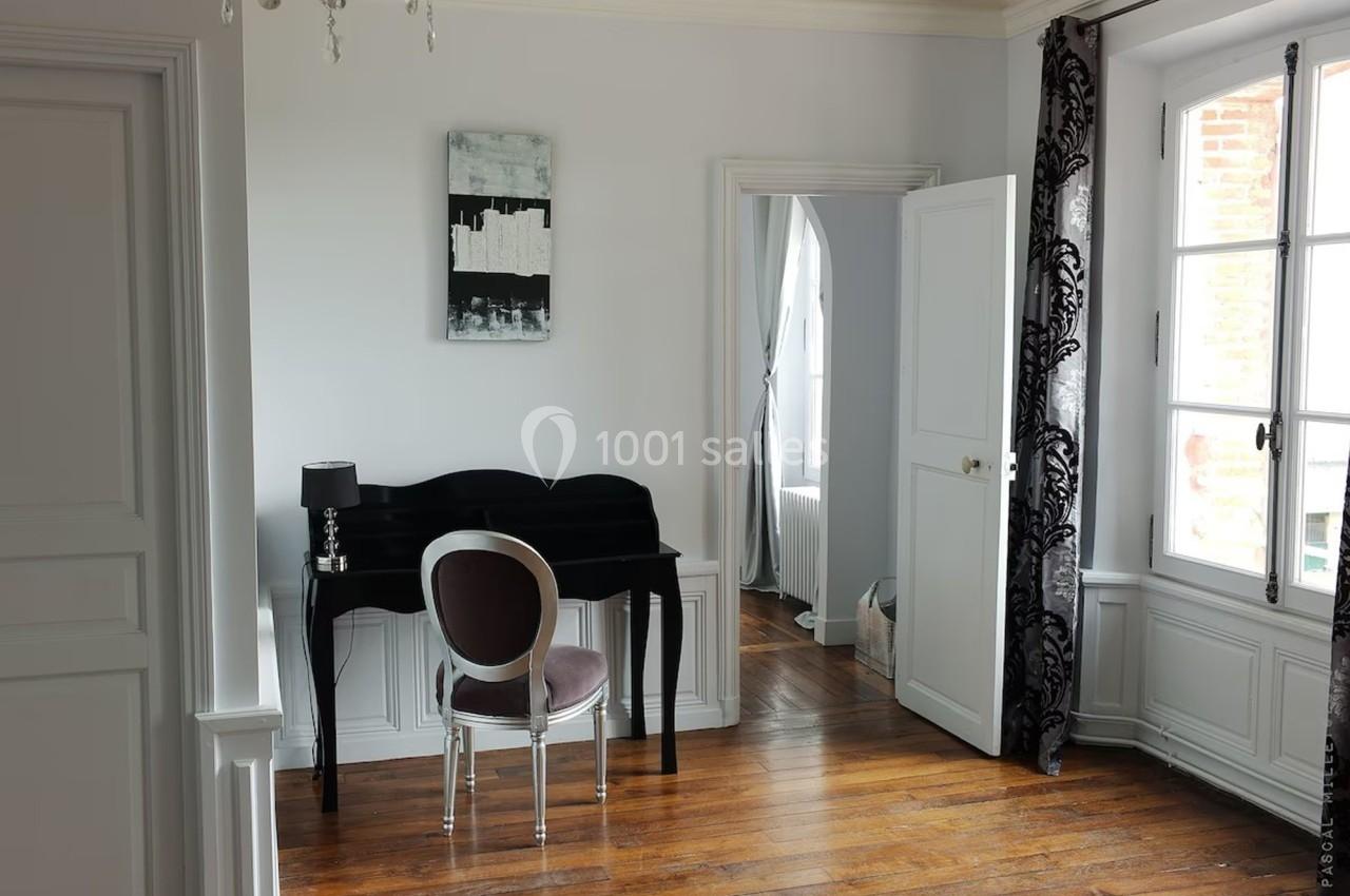 Bureau noir avec chaise argentée dans une pièce lumineuse au parquet en bois, près d'une fenêtre et d'une porte ouverte.