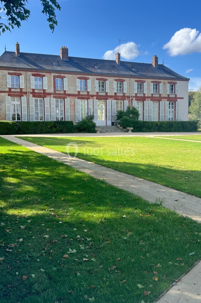 Grande maison à deux étages avec des volets rouges, entourée d'une pelouse et d'allées sous un ciel dégagé.