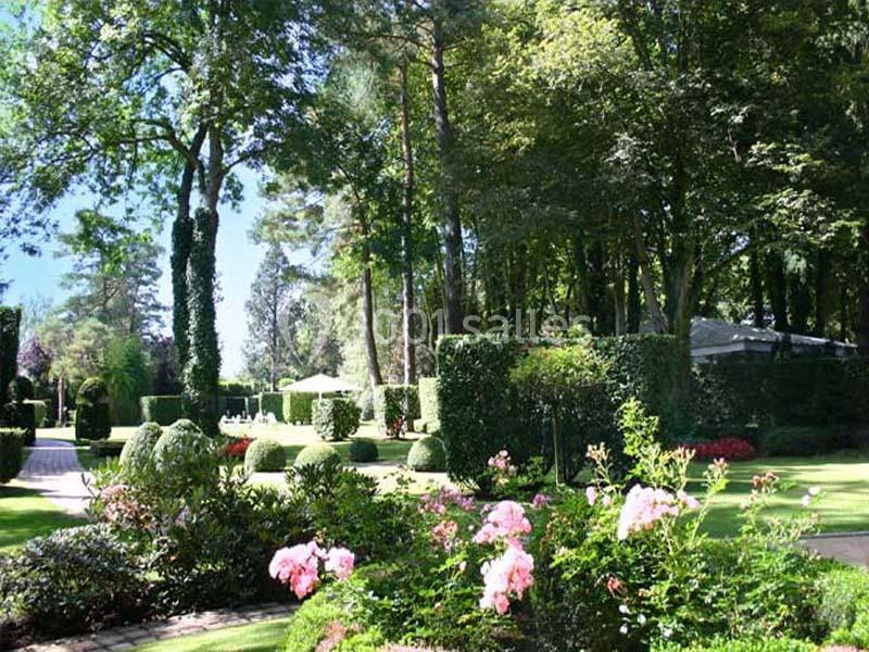 Jardin paysager avec pelouse, massifs de fleurs, arbustes taillés et arbres sous un ciel dégagé.