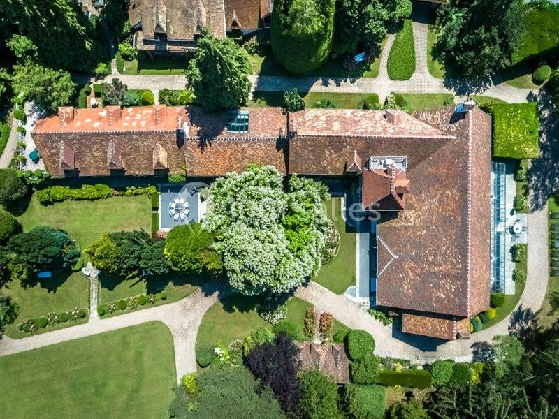 Vue aérienne d'une grande maison avec toit en tuiles, entourée de jardins paysagers et de chemins en gravier.