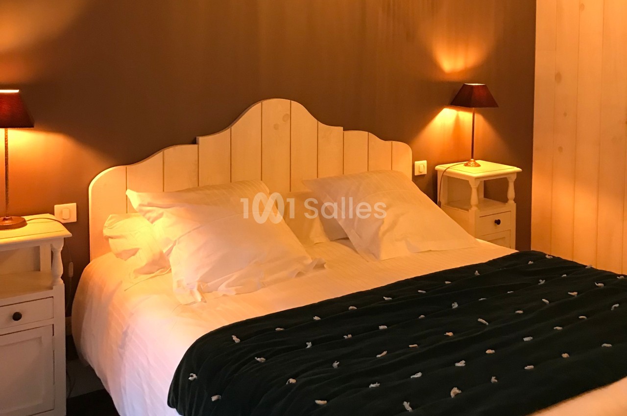 Lit double avec tête de lit en bois, couvert d'une couette sombre, entouré de tables de chevet et lampes allumées.