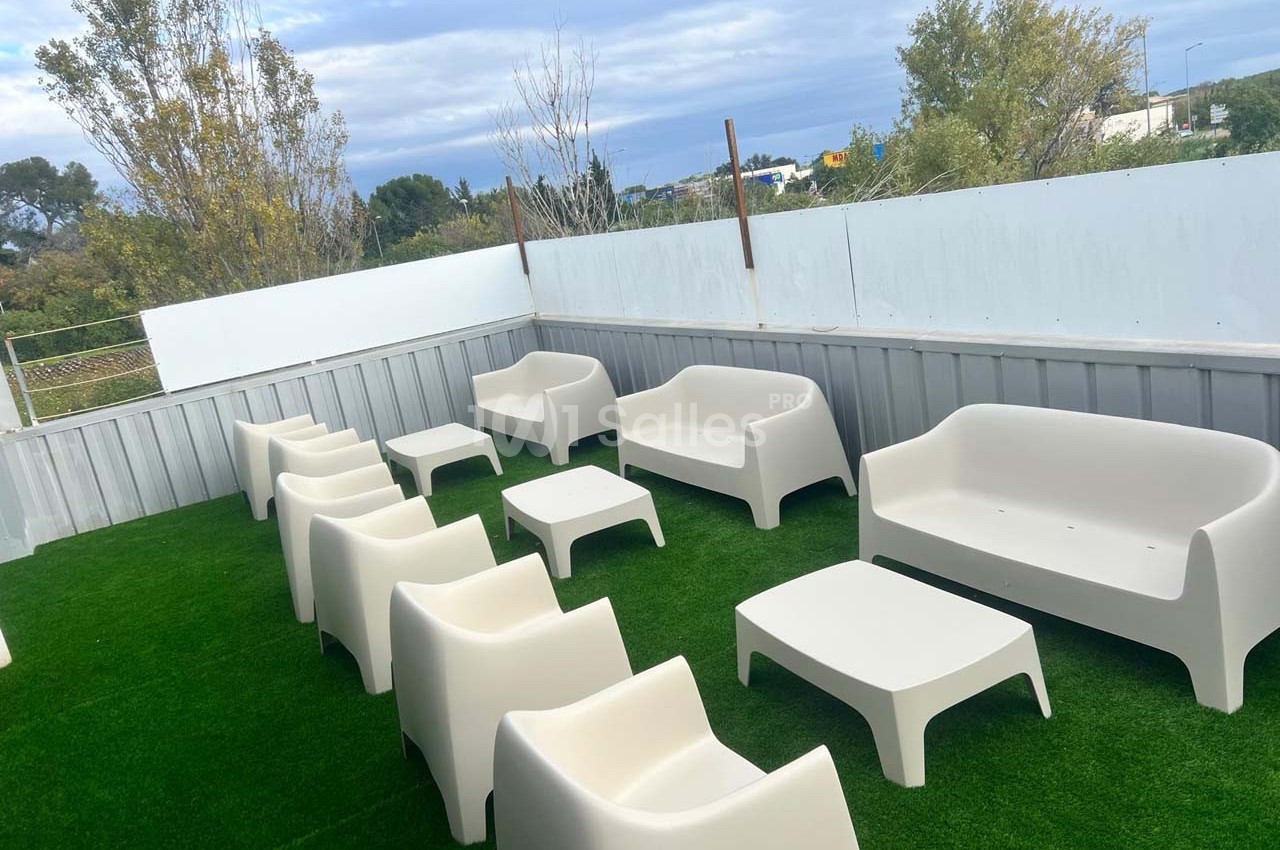 Mobilier de jardin blanc composé de fauteuils et tables basses disposés sur une terrasse avec pelouse synthétique.