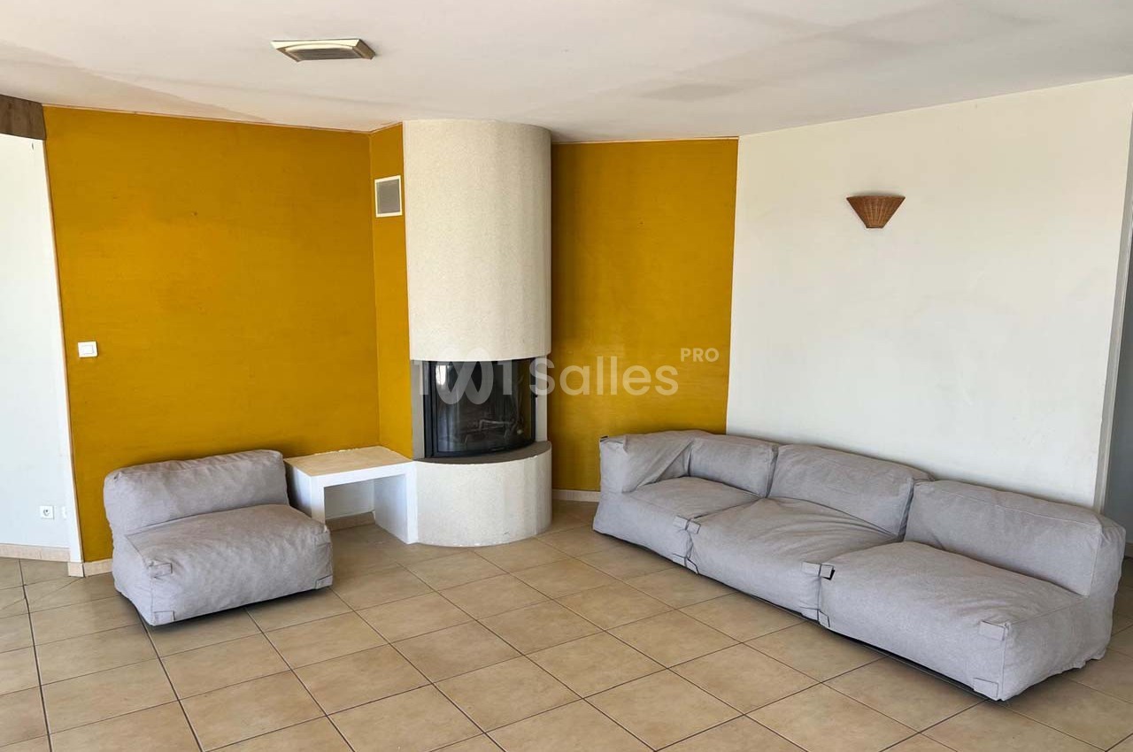 Salon avec murs jaunes, cheminée d'angle blanche, canapé gris en L et sol en carrelage beige.