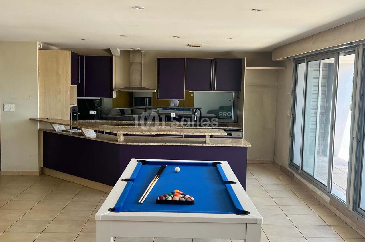 Cuisine moderne avec meubles violets, plan de travail en marbre, et table de billard blanche au premier plan.