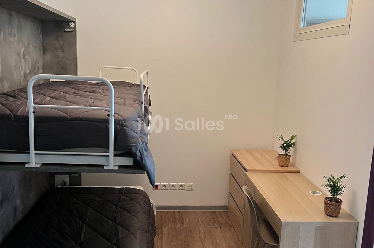 Chambre avec lits superposés, bureau en bois, deux petites plantes et une fenêtre apportant de la lumière naturelle.