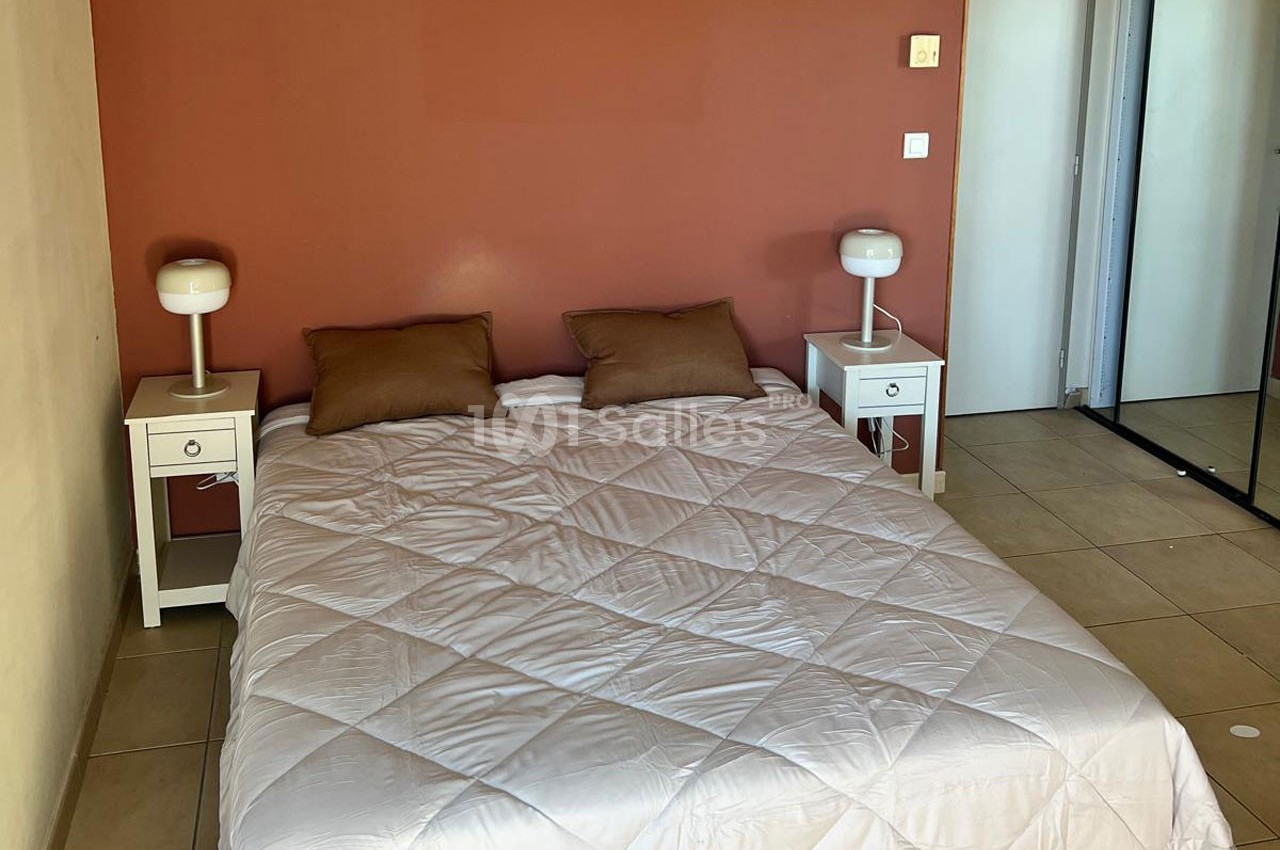 Lit double avec une couette blanche, deux oreillers bruns, tables de chevet blanches et lampes, mur rouge en arrière-plan.
