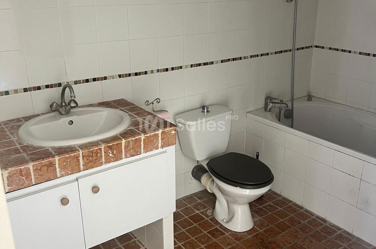 Salle de bain avec lavabo sur meuble en carrelage, toilettes, baignoire et murs carrelés blancs.