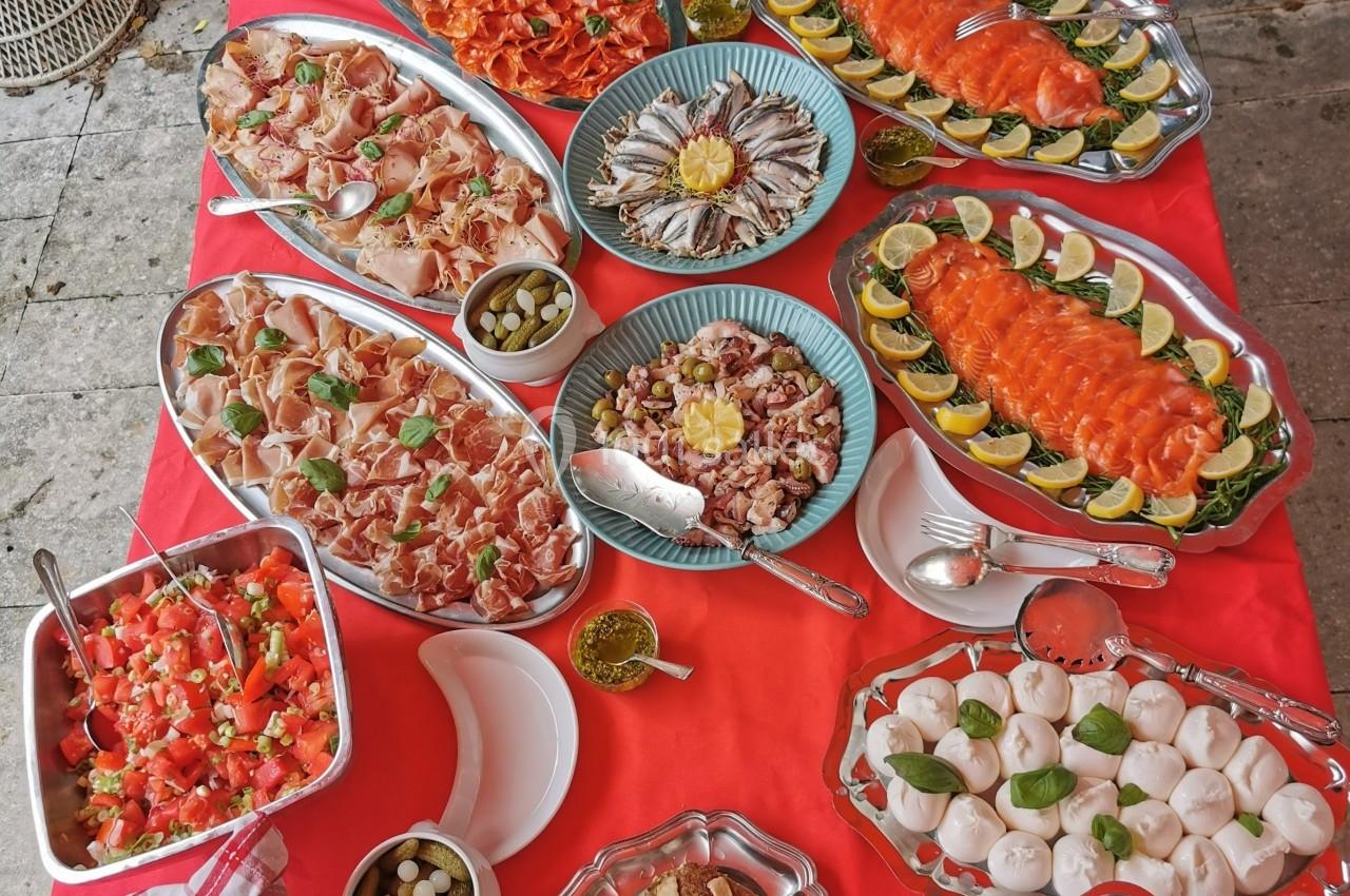 Buffet varié avec charcuterie, fruits de mer, légumes, sauces et pains disposés sur une nappe rouge en extérieur.