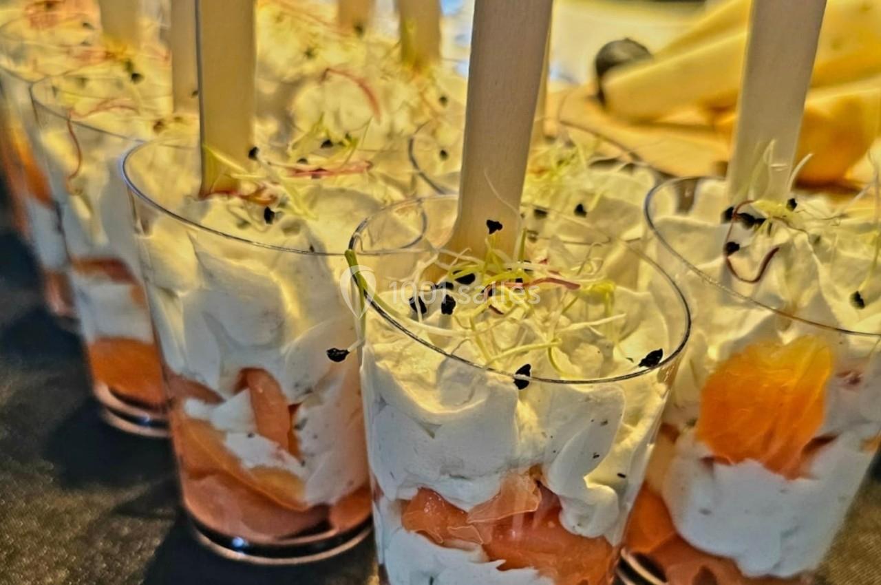 Verrines de saumon fumé, crème fouettée et pousses germées, servies avec des bâtonnets en bois.