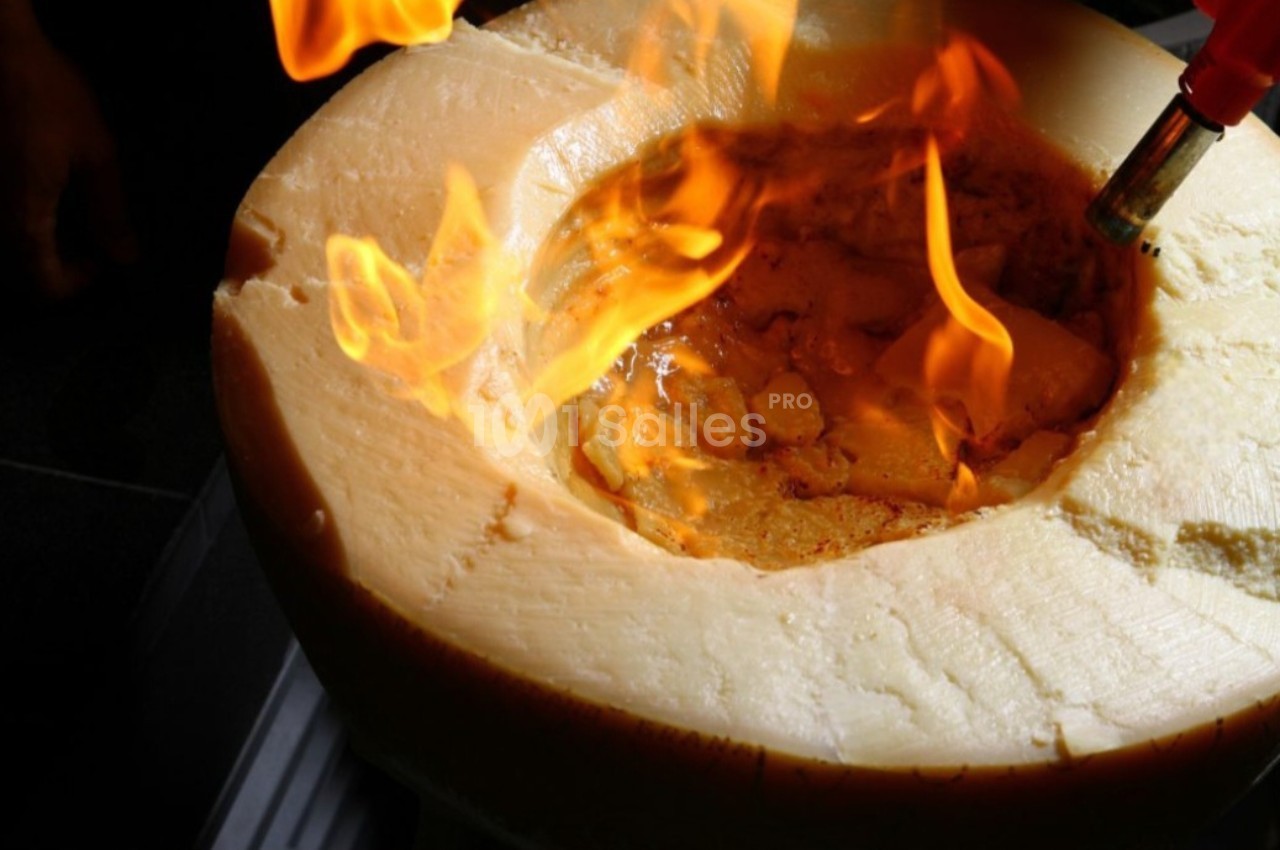 Fromage creusé enflammé par un chalumeau, utilisé pour une préparation culinaire.