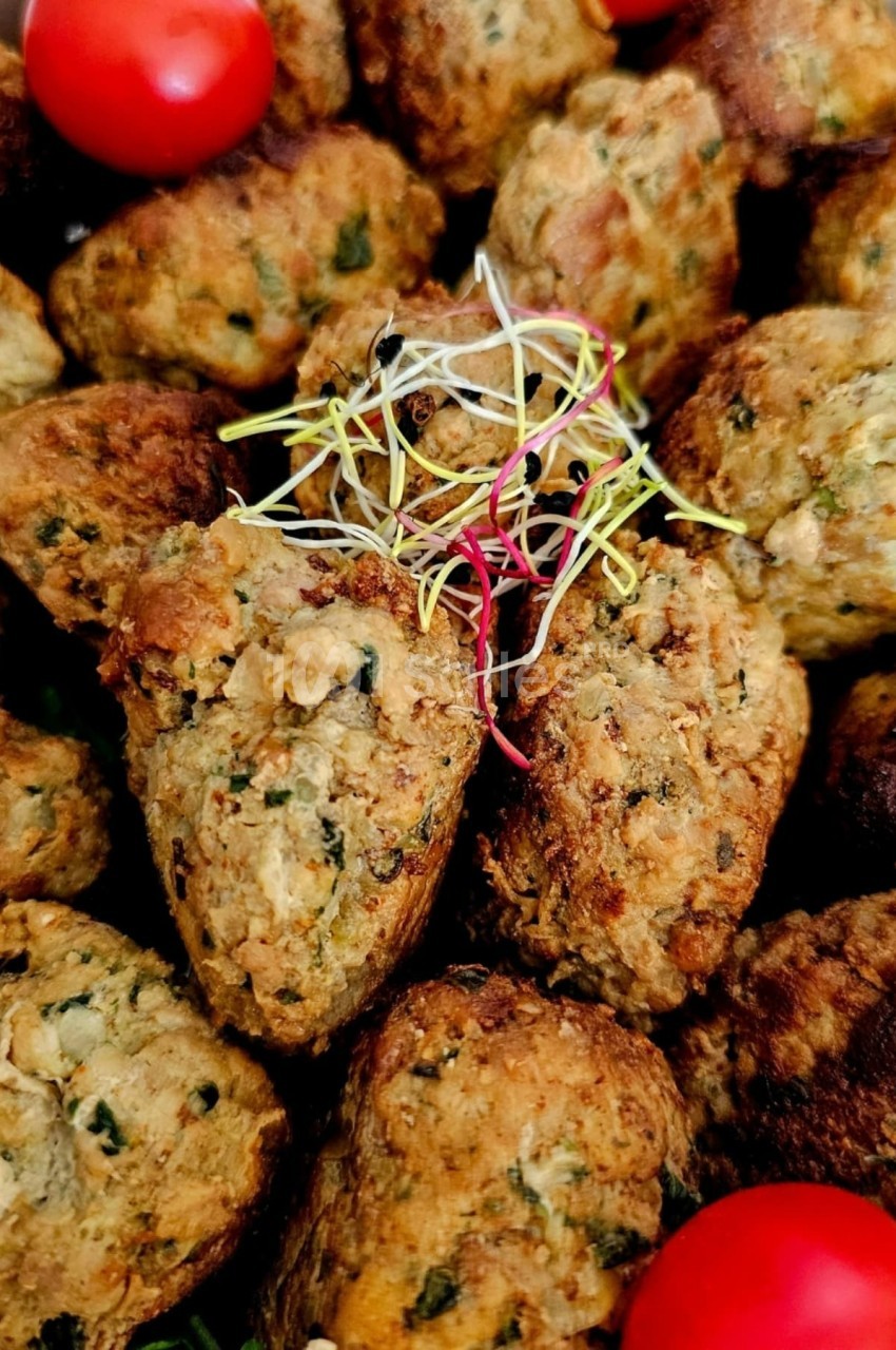 Boulettes végétariennes dorées garnies de jeunes pousses et accompagnées de tomates cerises rouges.