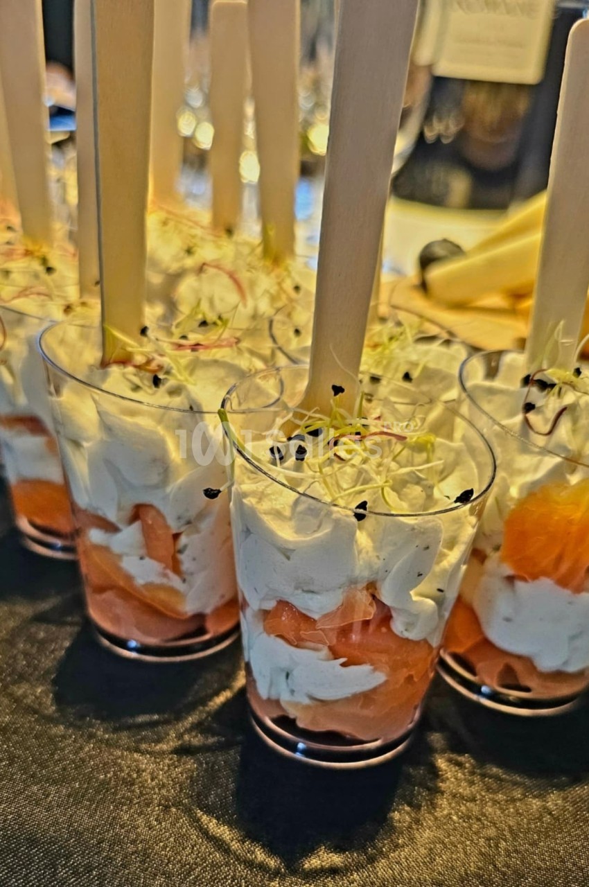 Verrines de saumon fumé, crème fouettée et pousses germées, servies avec des bâtonnets en bois.