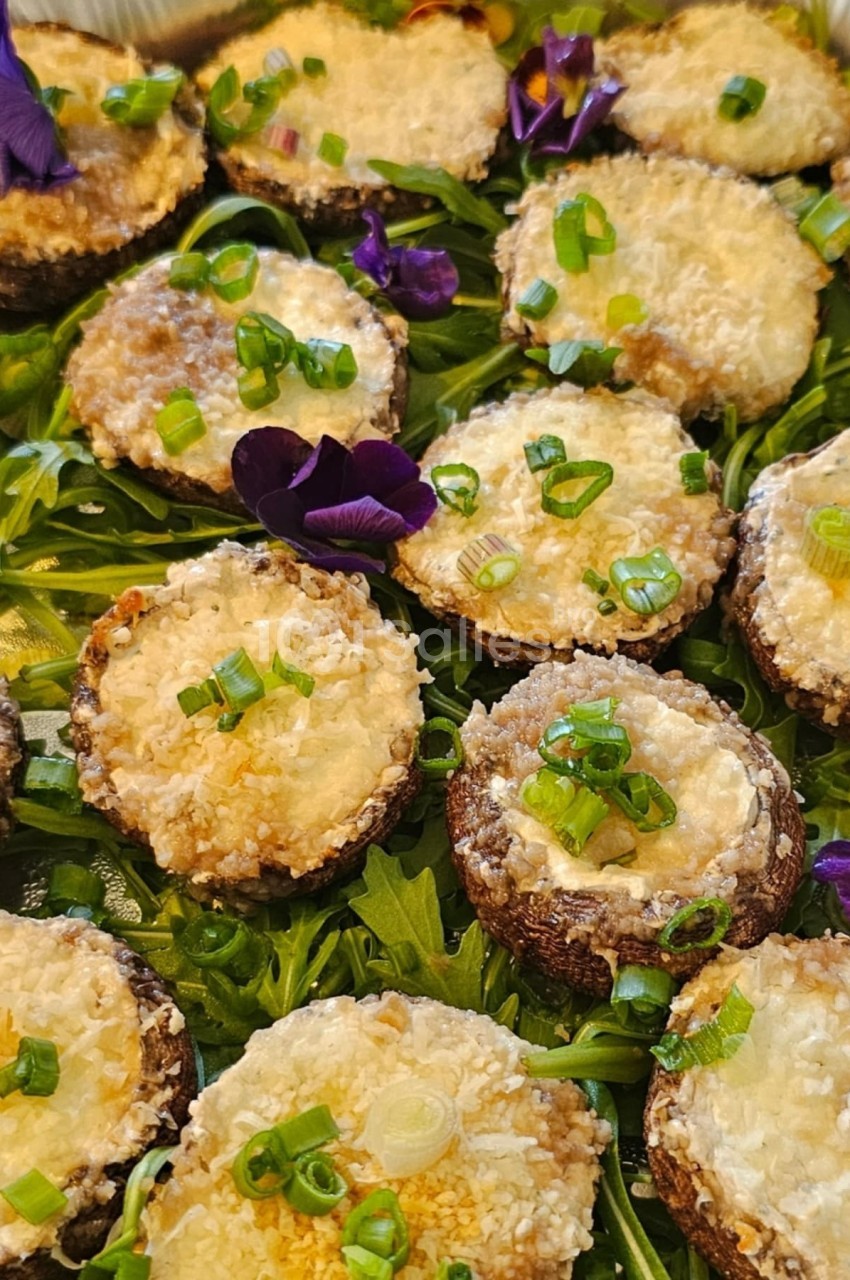 Champignons farcis gratinés sur un lit de roquette, garnis de ciboulette et de fleurs comestibles.