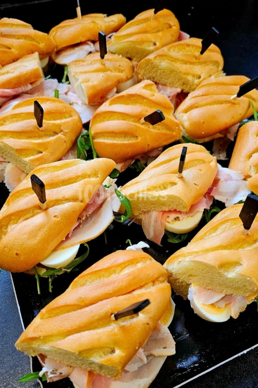 Plateau de mini-sandwichs garnis de jambon, œufs durs, roquette et servis sur pain doré.