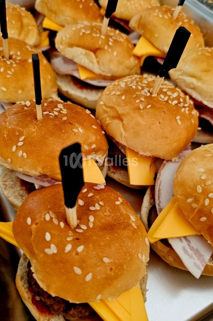 Mini burgers garnis de fromage, jambon et piques en bois, disposés dans un plateau en métal.
