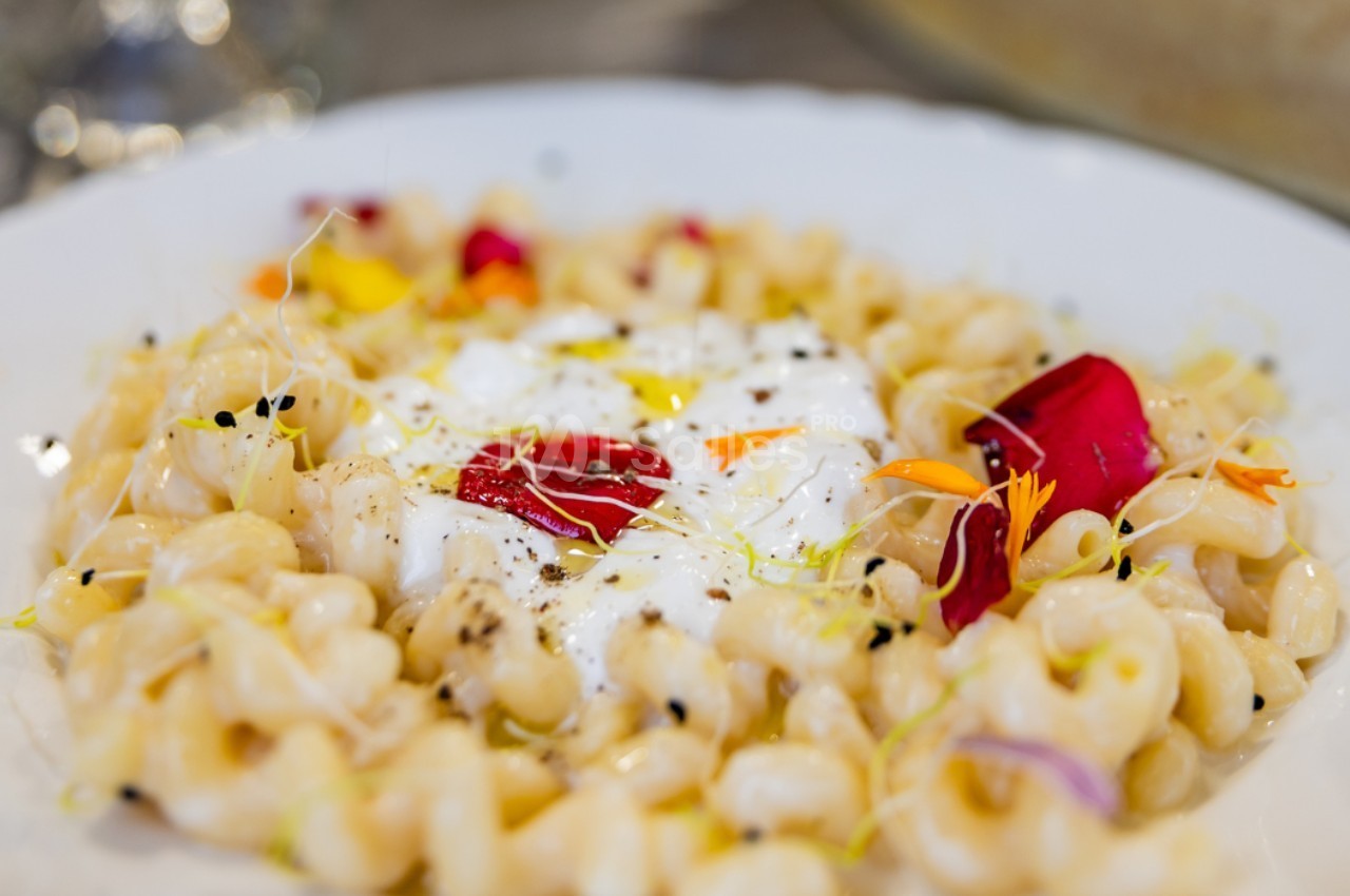 Assiette de pâtes crémeuses garnies de fleurs comestibles, de graines et de fromage frais au centre.