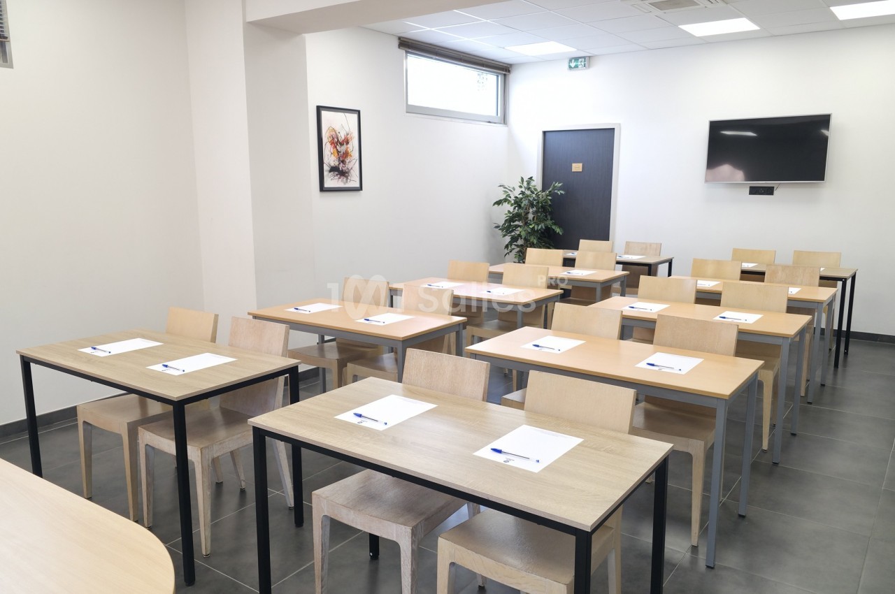 Salle de formation lumineuse avec des tables en bois, des chaises alignées, des blocs-notes et un écran mural.