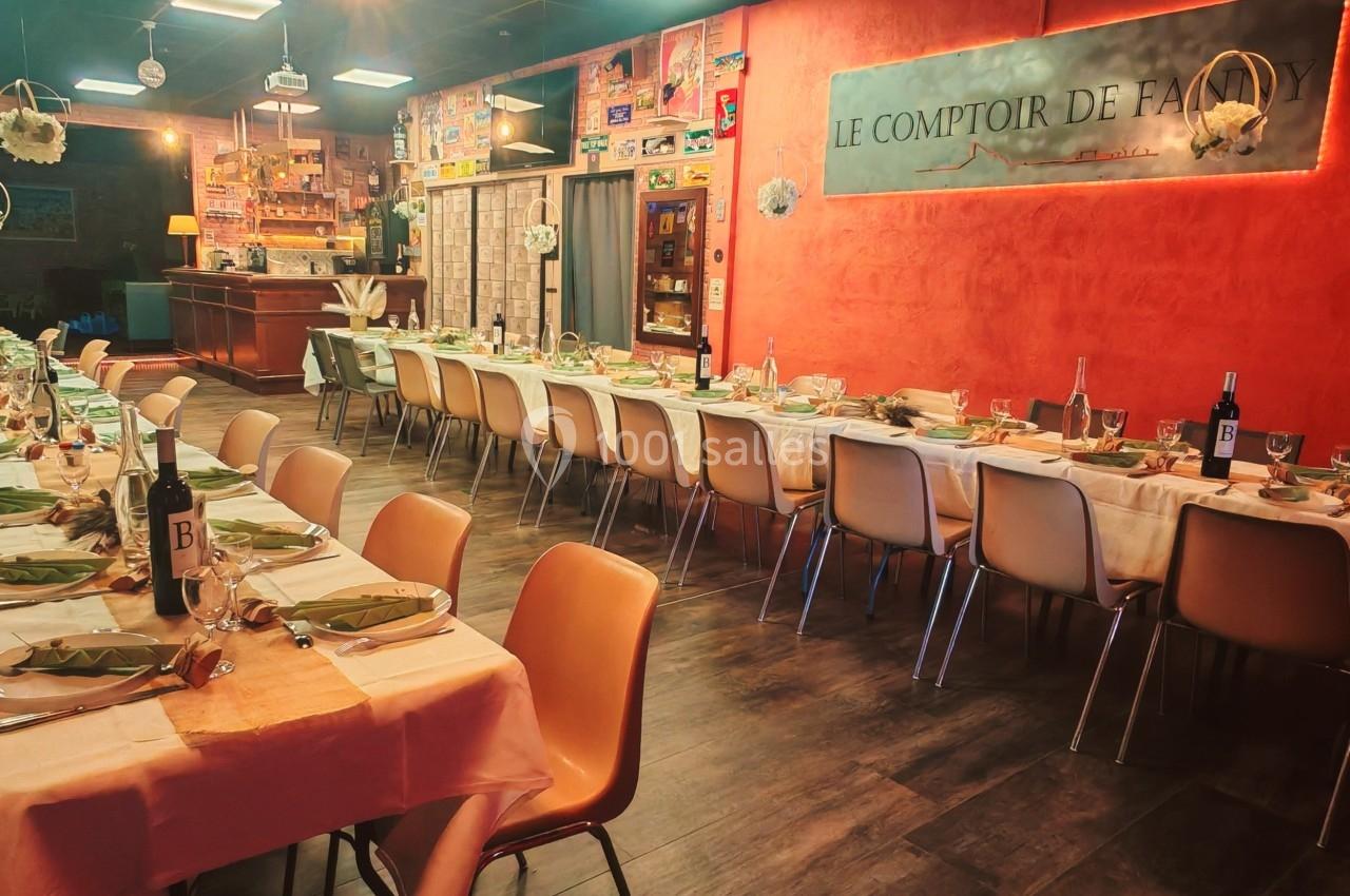 Salle de restaurant avec longues tables dressées, chaises alignées et décoration lumineuse dans une ambiance chaleureuse.