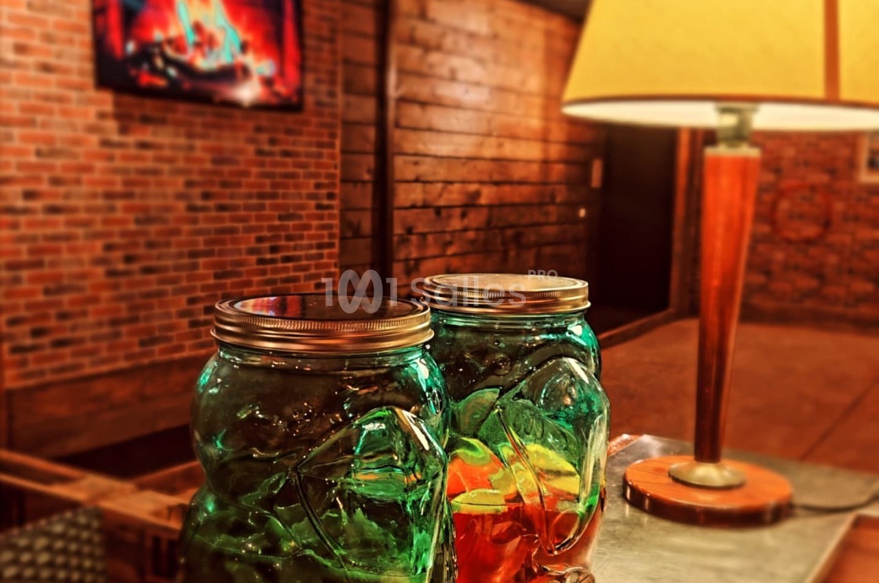 Deux bocaux en verre contenant des boissons colorées sur un comptoir, avec une lampe et un écran affichant une cheminée en…