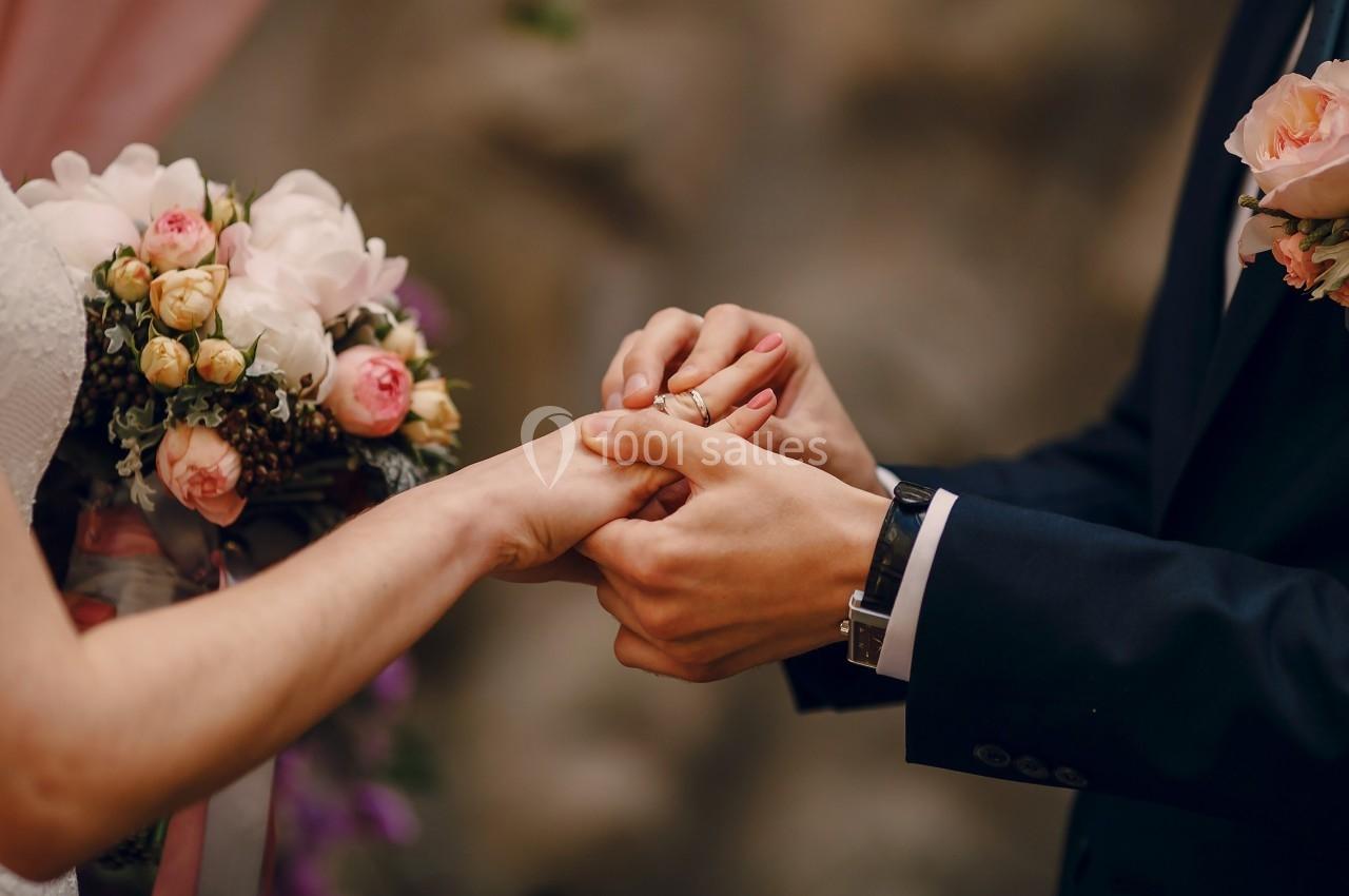 Un couple échange des alliances lors d'une cérémonie de mariage, avec un bouquet de fleurs en arrière-plan.
