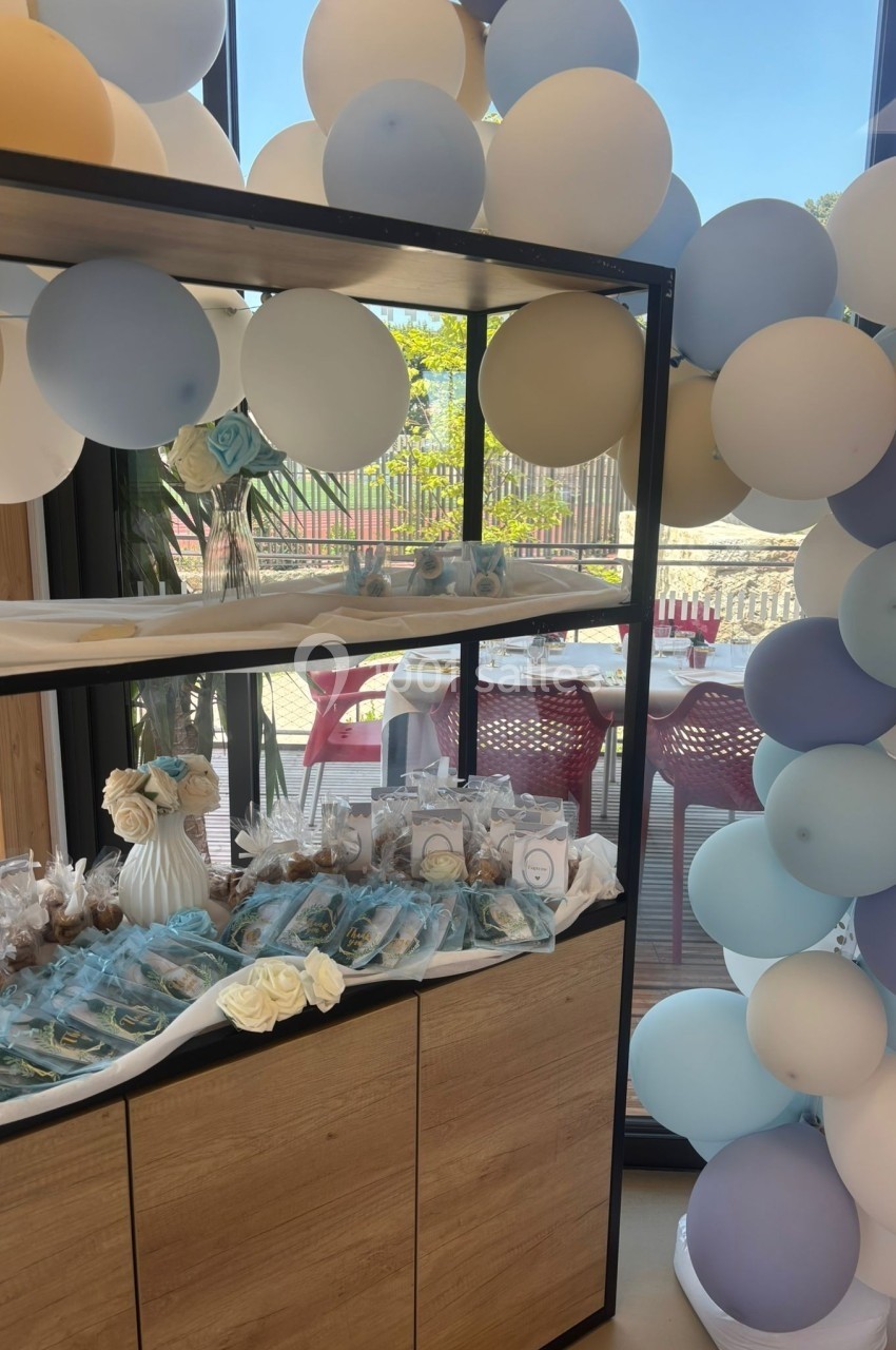 Décoration avec ballons pastel et table garnie de douceurs dans un espace lumineux avec vue sur l'extérieur.