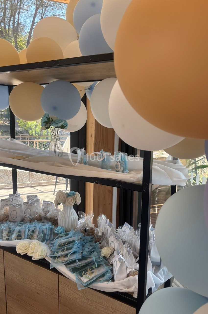 Décoration de fête avec ballons pastel, étagère contenant des cadeaux emballés et des accessoires bleus et blancs.