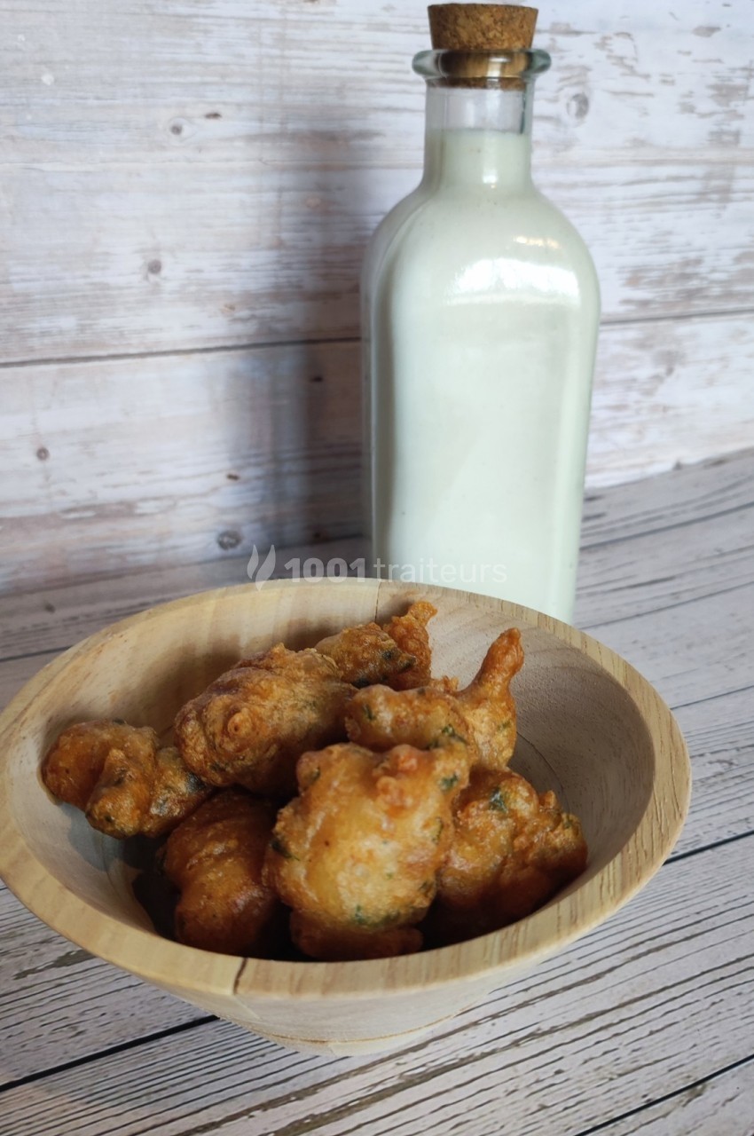 Beignets dorés dans un bol en bois devant une bouteille en verre remplie de liquide blanc.