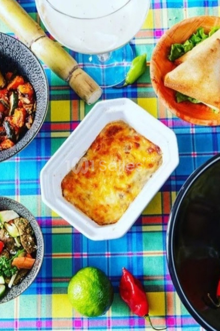 Repas coloré composé de plats créoles variés, avec légumes, gratin, samoussas, canne à sucre et piments sur une nappe à…