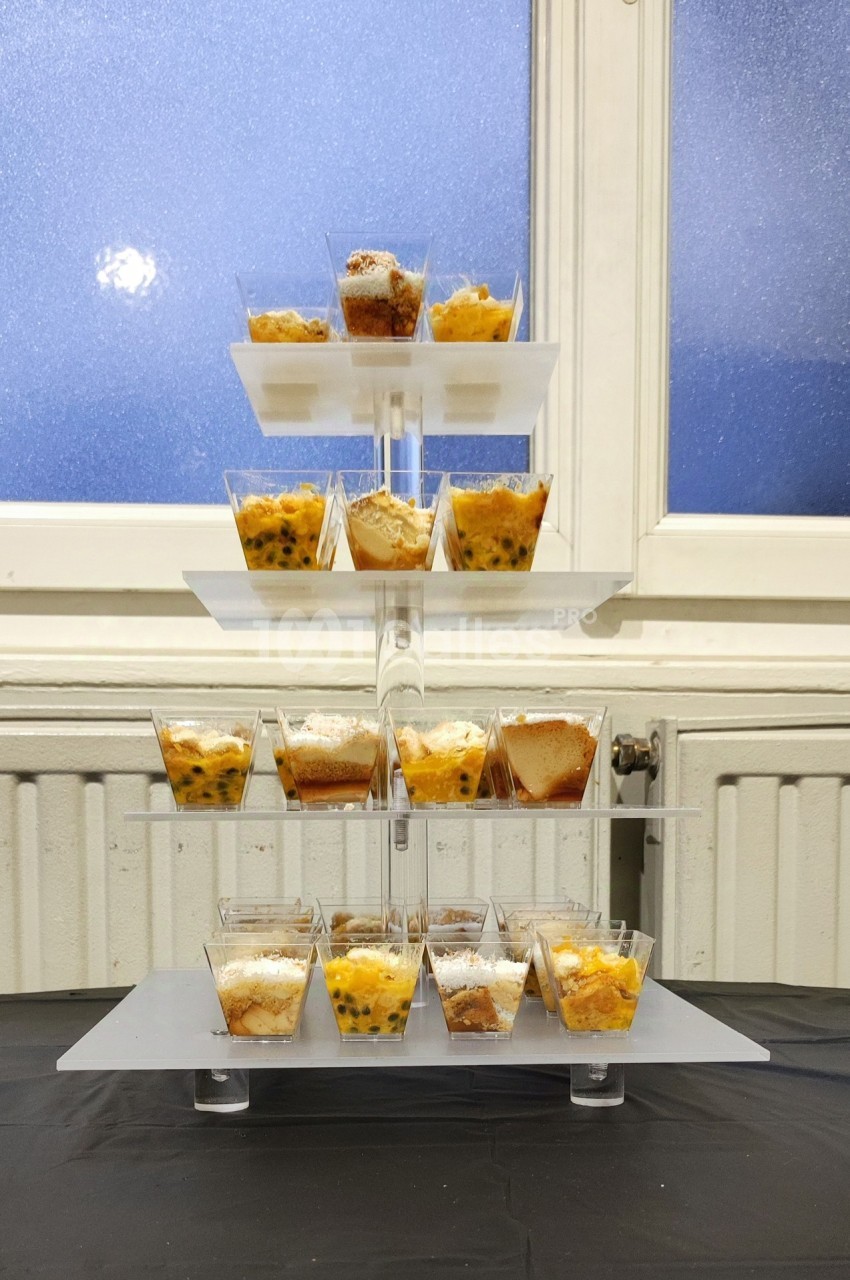 Présentoir à étages avec des verrines de desserts variés, placé devant une fenêtre givrée.