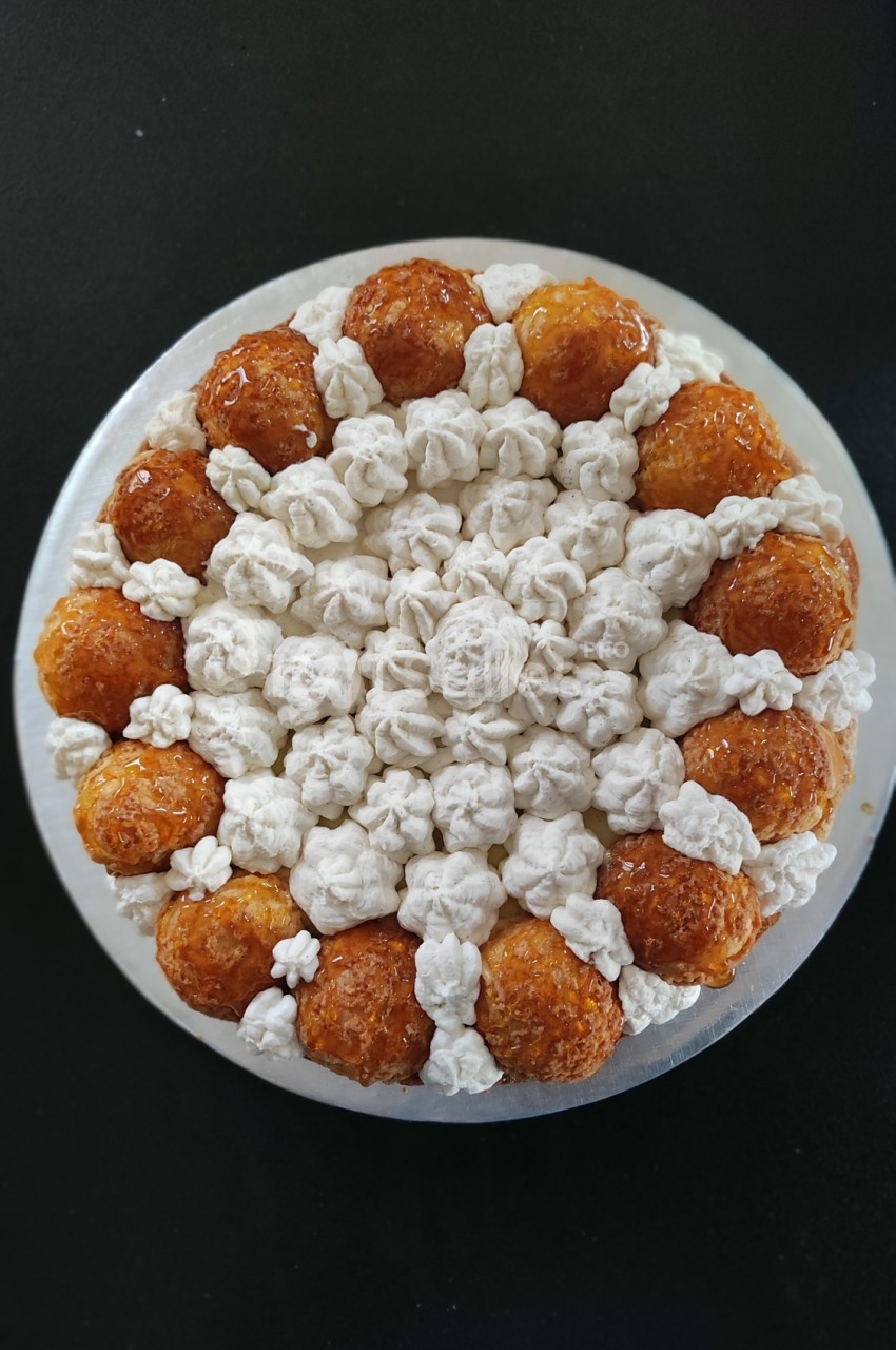 Gâteau composé de choux caramélisés et de crème disposés en cercle sur un fond noir.