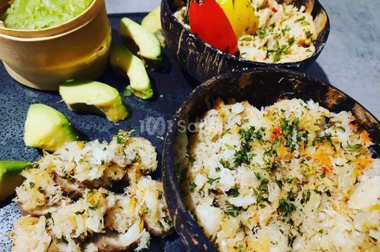 Assiettes de crabe émietté assaisonné, servies dans des coques de noix de coco avec des tranches d'avocat et une sauce verte.