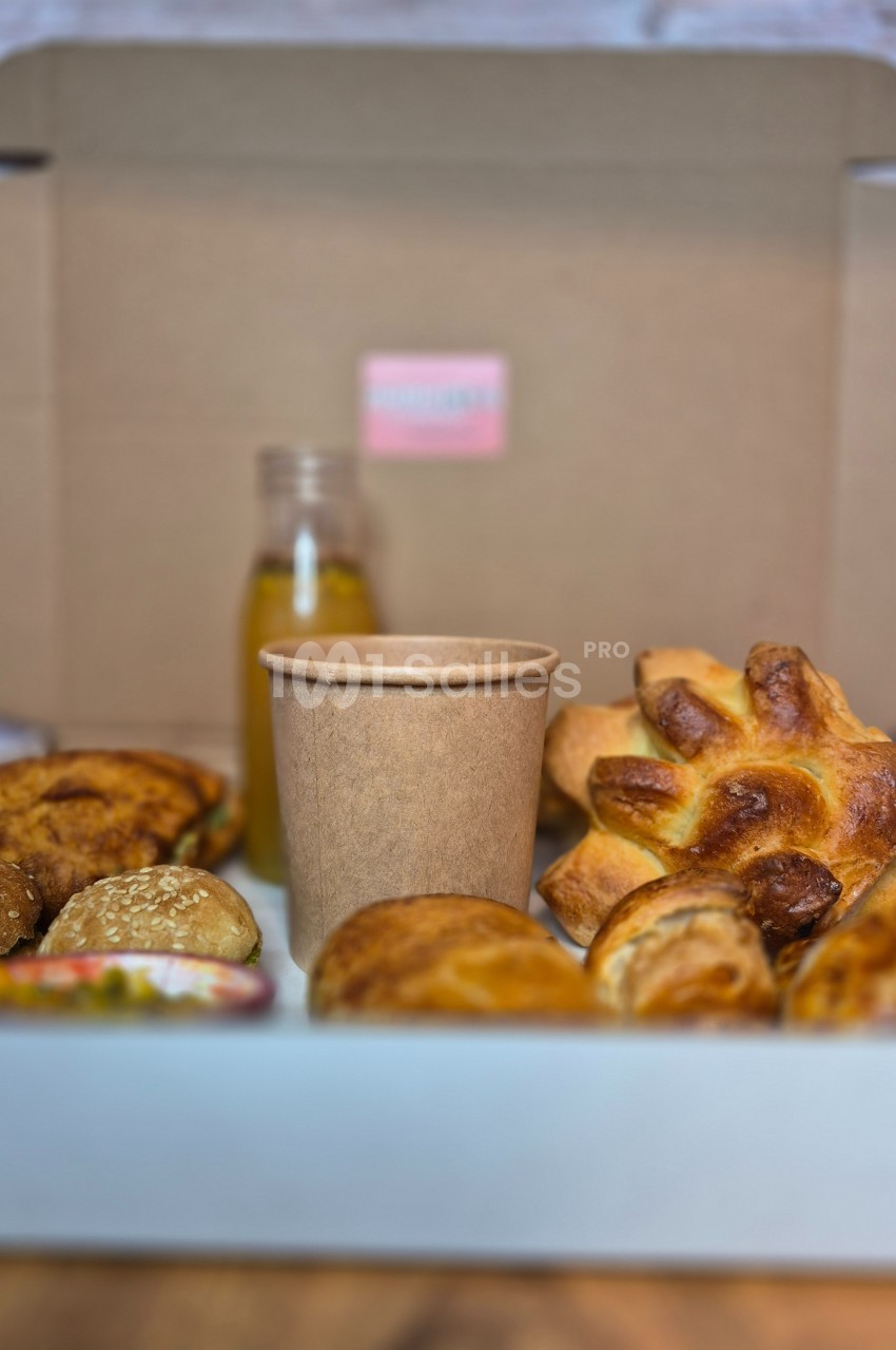 Assortiment de viennoiseries et pain avec une boisson dans un gobelet en carton et une bouteille en arrière-plan.
