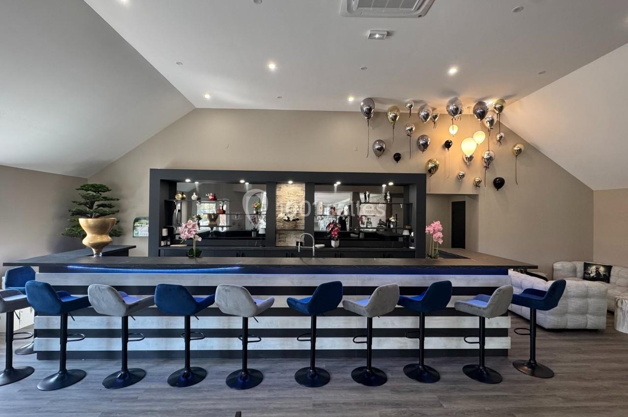 Salle moderne avec un long bar, tabourets alignés, décoration murale avec ballons et éclairage tamisé.
