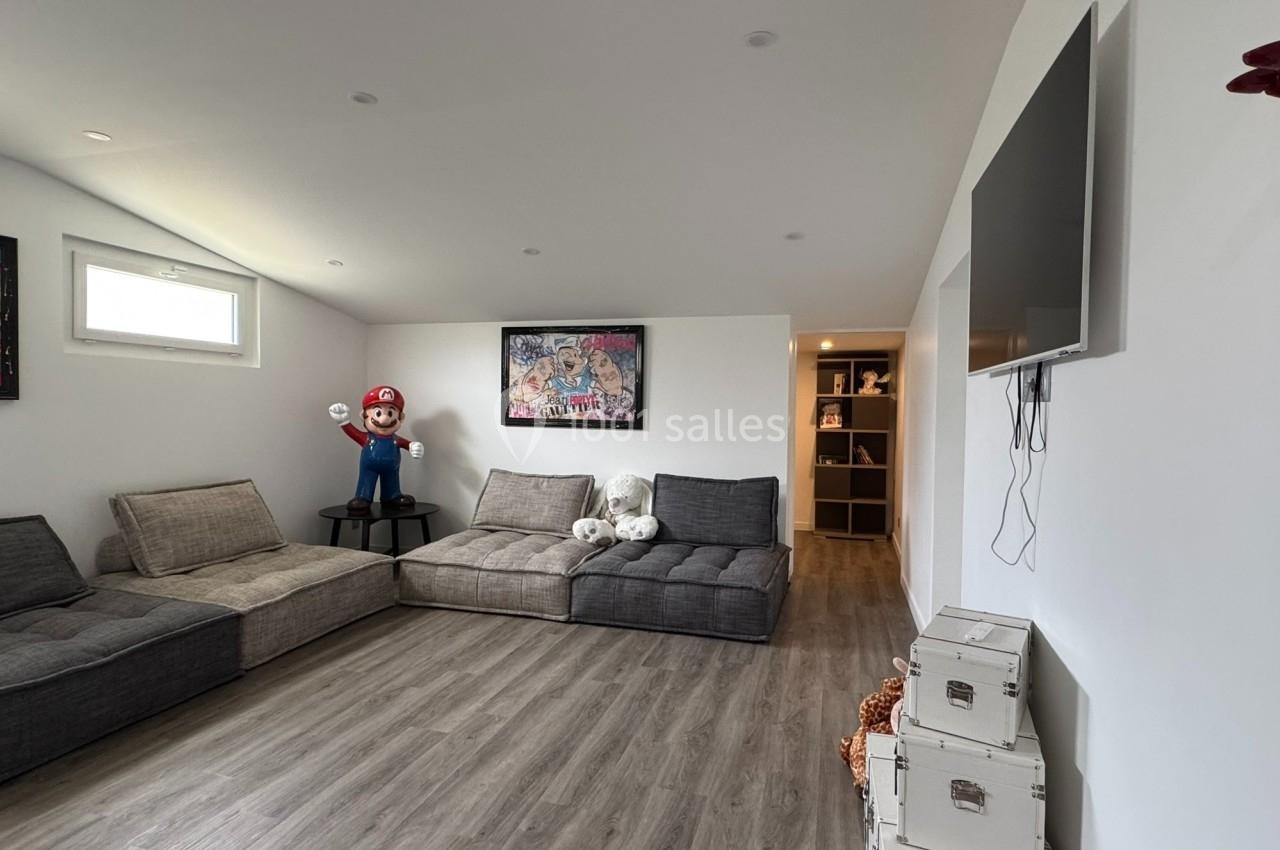 Salle de détente avec canapés gris, figurine décorative, cadres accrochés, télévision murale et sol en parquet.