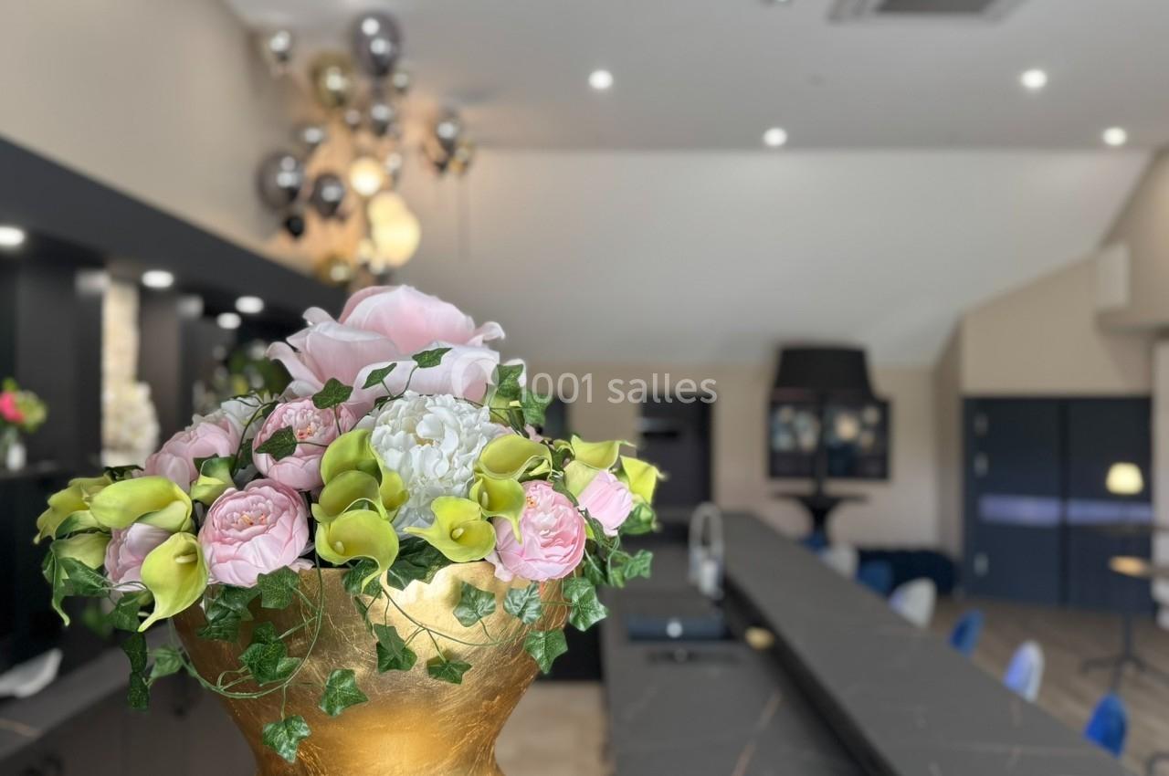 Arrangement floral coloré dans un vase doré, placé sur un comptoir dans un espace intérieur moderne et lumineux.