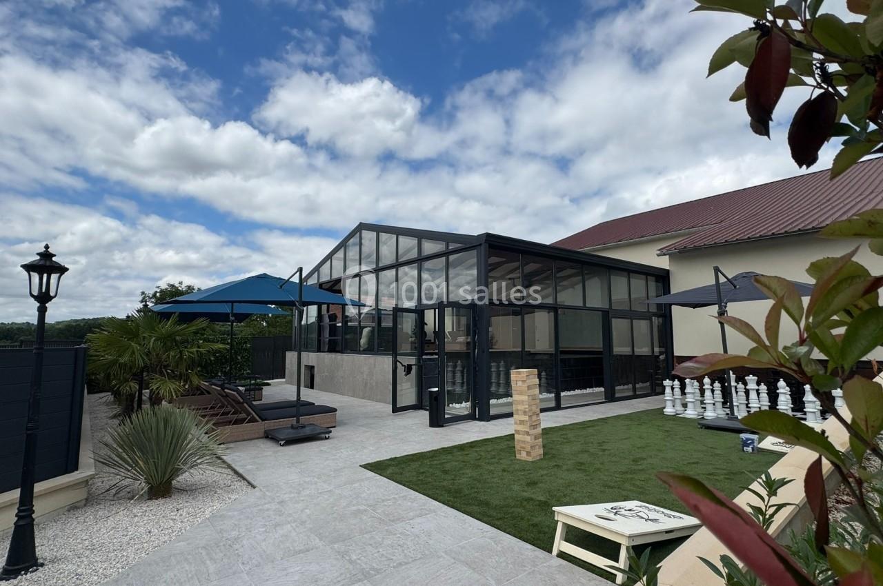 Véranda moderne en verre donnant sur une terrasse aménagée avec mobilier, pelouse artificielle et jeux extérieurs.