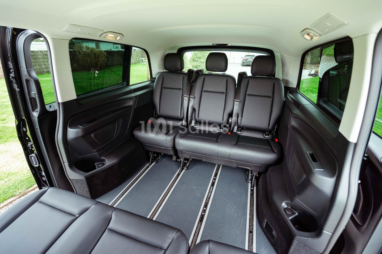 Intérieur d'un véhicule spacieux avec trois rangées de sièges noirs en cuir et un espace dégagé au sol.
