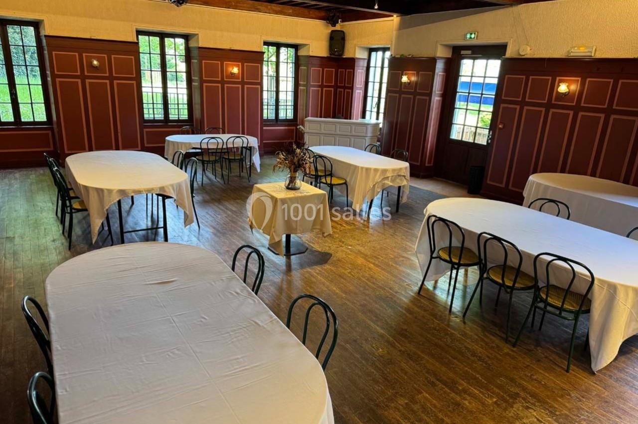 Salle avec des tables rondes et rectangulaires recouvertes de nappes blanches, entourées de chaises noires.
