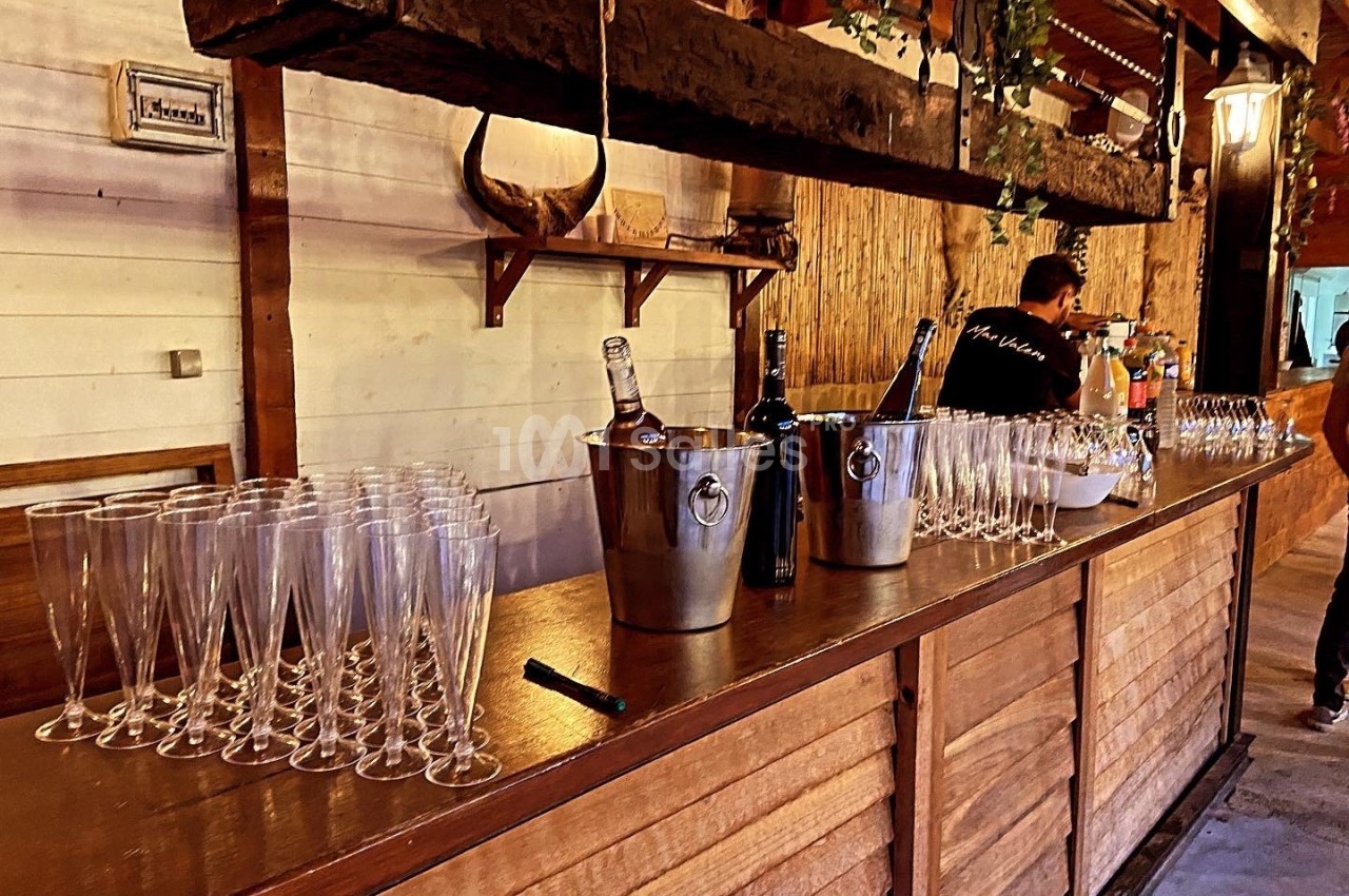 Comptoir en bois avec verres à pied alignés, seaux à glace contenant des bouteilles et un homme en arrière-plan.