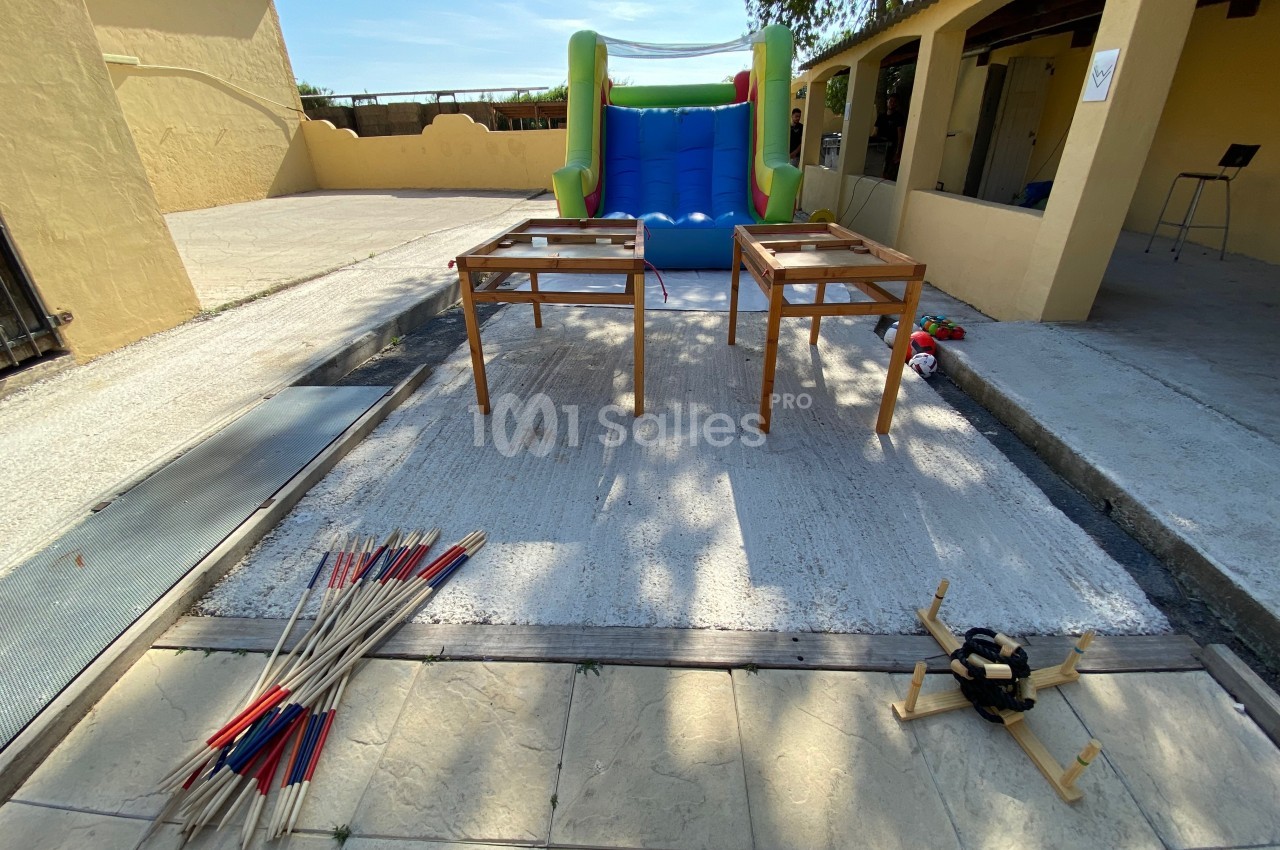 Deux tables en bois devant un jeu gonflable coloré, avec des mikados géants et un jeu d'adresse au sol.