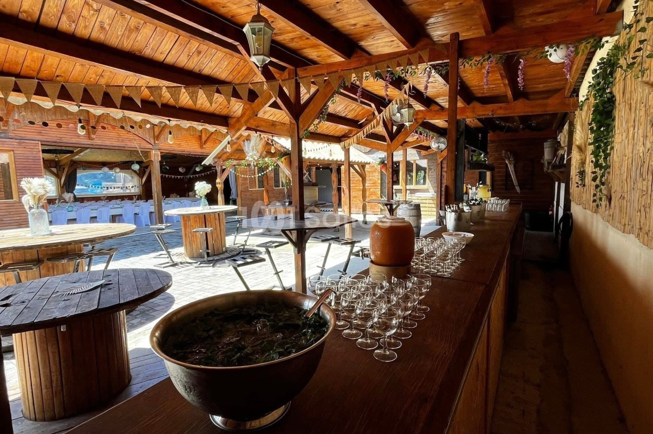 Salle en bois avec tables rondes, bar garni de verres et d'une grande coupe, décorée pour un événement festif.