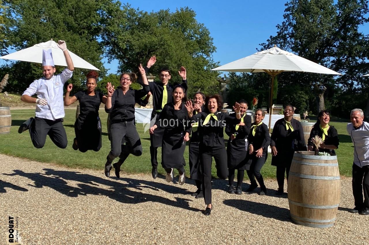 Un groupe de personnes en uniforme noir saute en l'air dans un espace extérieur ensoleillé avec parasols et tonneaux.